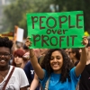 A young woman holds a People over Profit banner at a demonstration